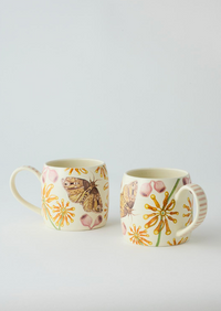 Behind The Trees - Two ceramic mugs with floral and butterfly designs on a light gray background - Angus & Celeste Buttermilk Mugs - Firewheel Tree