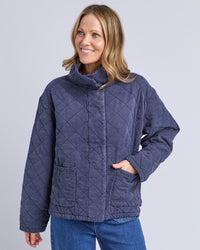 Behind The Trees - Woman wearing a blue quilted jacket on a gray background - Elm - Aurora Quilted Jacket - Navy