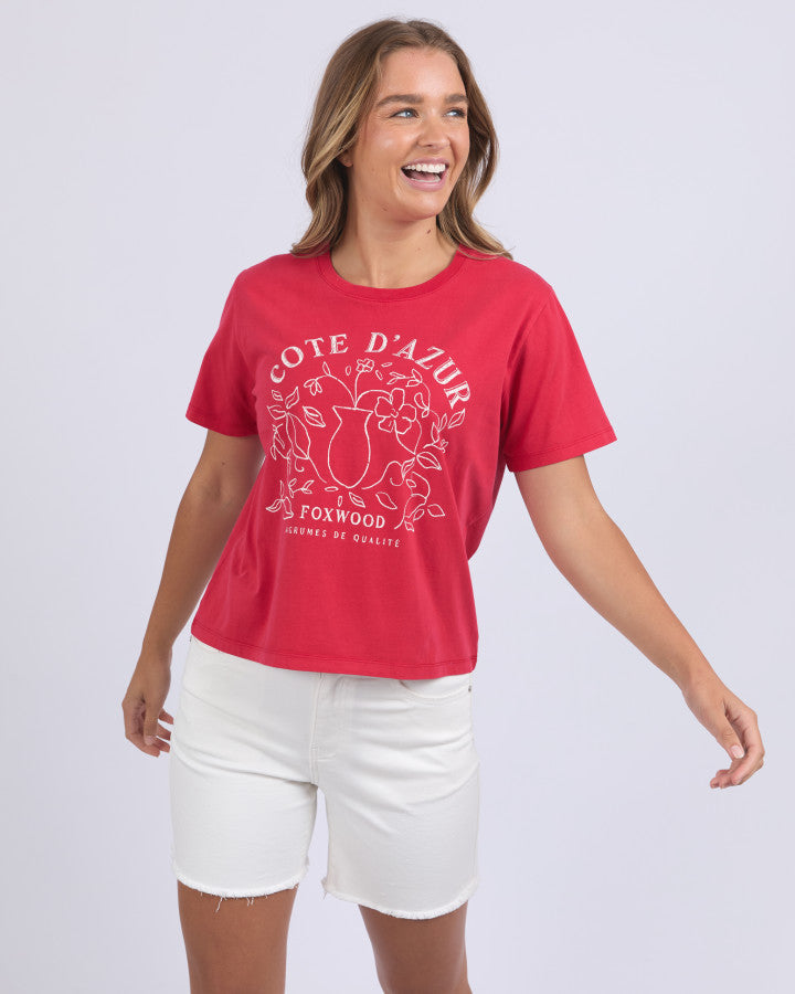 Behind The Trees - Woman wearing a red t-shirt with 'Cote d'Azur' design and white shorts on a light gray background