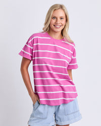 Behind The Trees - A woman wearing a pink short-sleeve t-shirt with white horizontal stripes and light blue denim shorts, standing against a light gray studio background. - Elm - Halli Short Sleeve Tee - Stripe Pink & White