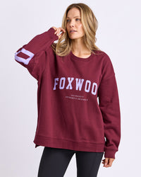Behind The Trees - Woman wearing a maroon 'FOXWOOD' sweatshirt and blue leggings on a light gray background -Foxwood - Interval Crew - Port with Lilac