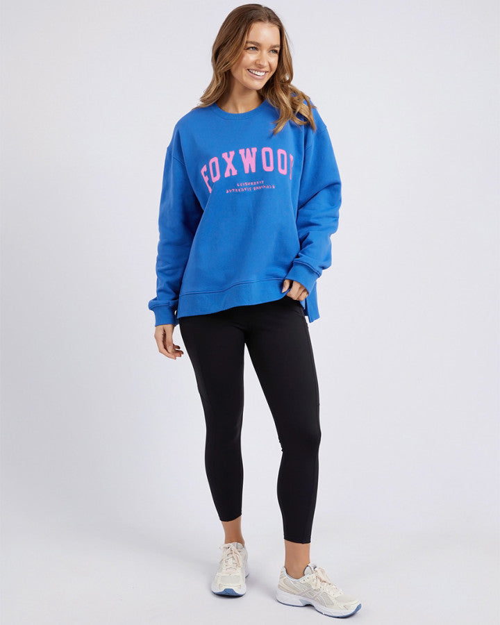 Behind The Trees - Woman wearing a blue sweatshirt with 'FOXWOOD' text on a white background - Foxwood - Interval Crew - Cobalt/Neon Pink