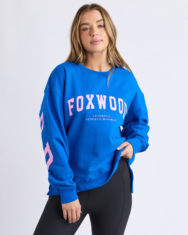 Behind The Trees - Woman wearing a blue sweatshirt with 'FOXWOOD' text on a white background - Foxwood - Interval Crew - Cobalt/Neon Pink