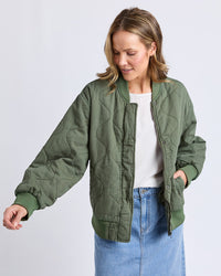 Behind The Trees -Woman wearing a green quilted jacket and blue jeans on a white background -Elm - Jean- Bomber Jacket- Clover