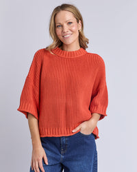 Behind The Trees - Woman wearing an orange sweater and blue jeans on a plain background - Elm - Luela Short Sleeve Knit - Orange