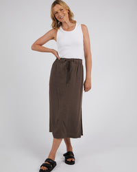 Behind The Trees - A woman modeling a brown midi skirt with a drawstring waist, paired with a white tank top and black slide sandals, against a light gray studio background. - Elm - Mila Utility Skirt - Chocolate