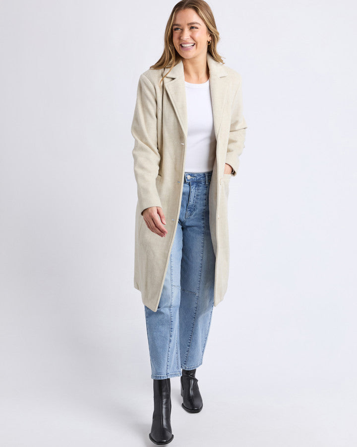 Behind The Trees - Woman wearing a beige coat, white shirt, and blue jeans on a white background - Foxwood - Nelson Coat - Oat