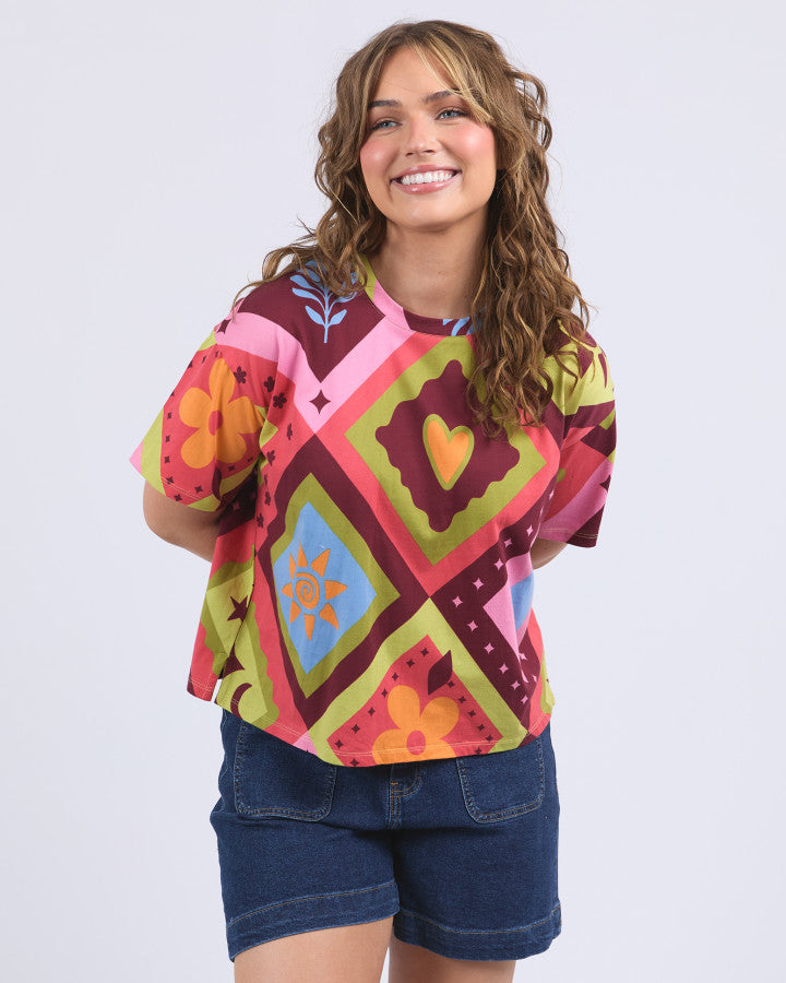 Behind The Trees - Elm - Rhode Tee - Woman wearing a colorful patterned shirt with a plain background -Multicoloured Yardage Print - 