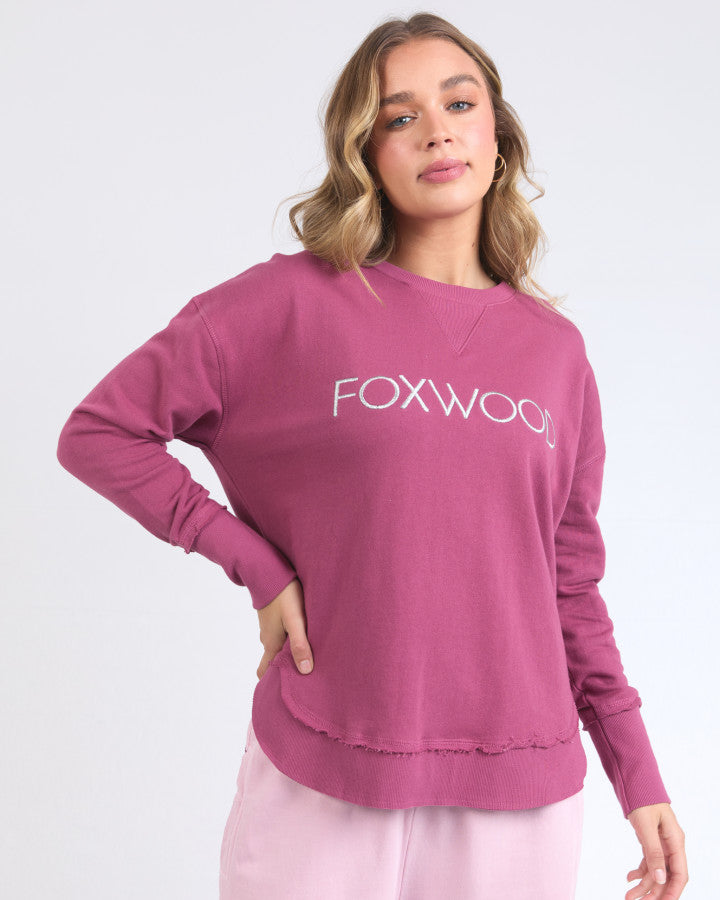 Behind The Trees - Woman wearing a pink sweatshirt with 'FOXWOOD' logo on a white background - Foxwood - Simplified Metallic Crew - Port With Silver