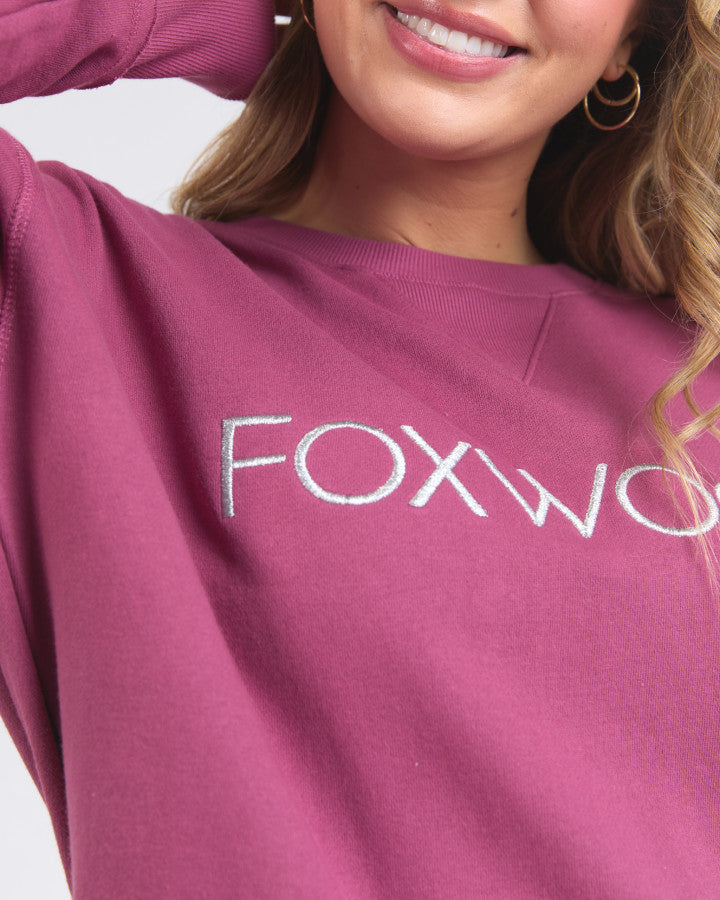 Behind The Trees - Woman wearing a pink sweatshirt with 'FOXWOOD' logo on a white background - Foxwood - Simplified Metallic Crew - Port With Silver