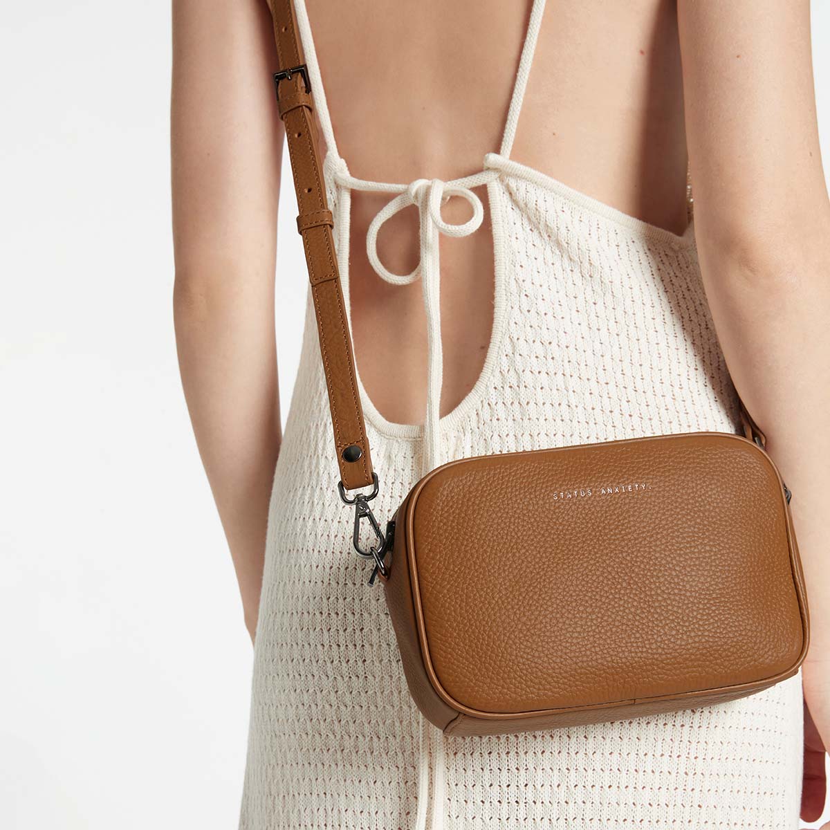 Behind The Trees - Brown leather crossbody bag with 'STATUS ANXIETY' branding on a white background - Status Anxiety - Plunder Bag - Camel