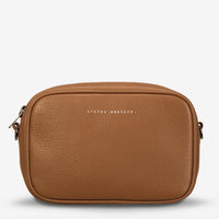 Behind The Trees - Brown leather crossbody bag with 'STATUS ANXIETY' branding on a white background - Status Anxiety - Plunder Bag - Camel